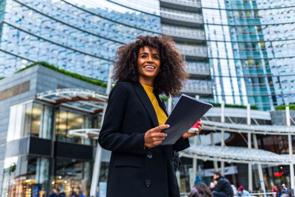 woman with black jacket and yellow top smiling with folder in hand